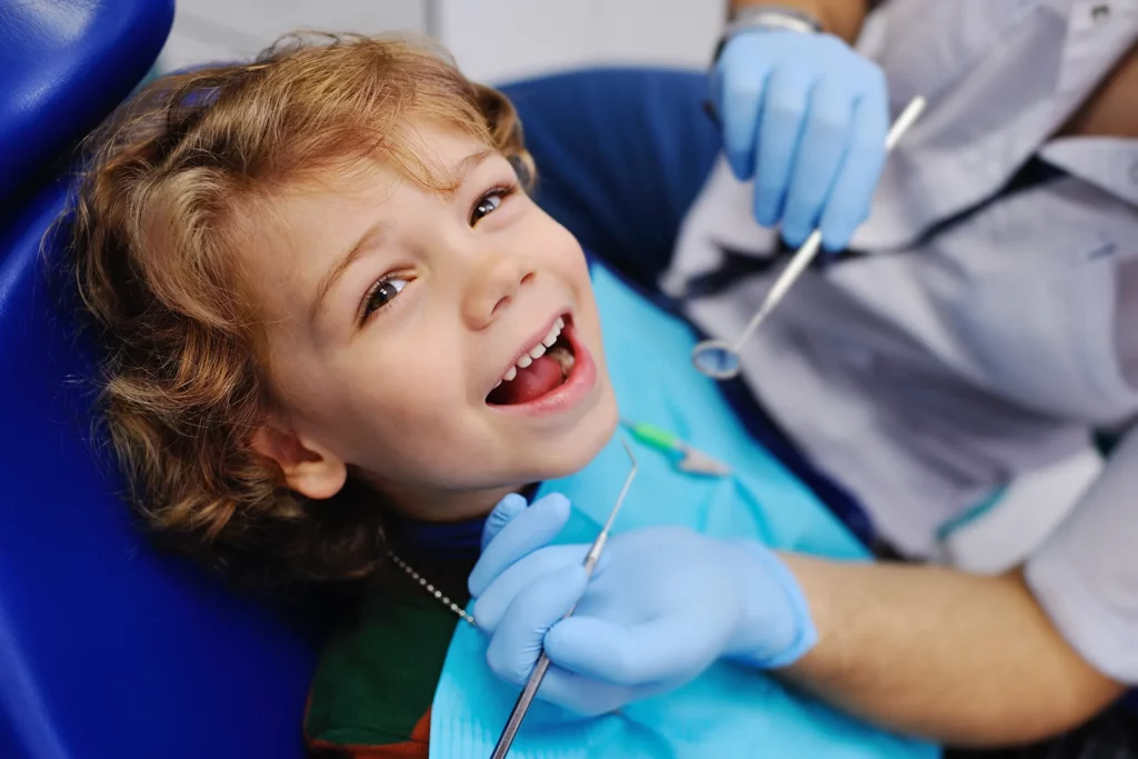 Smiling child sitting in a blue chair at the dental clinic.