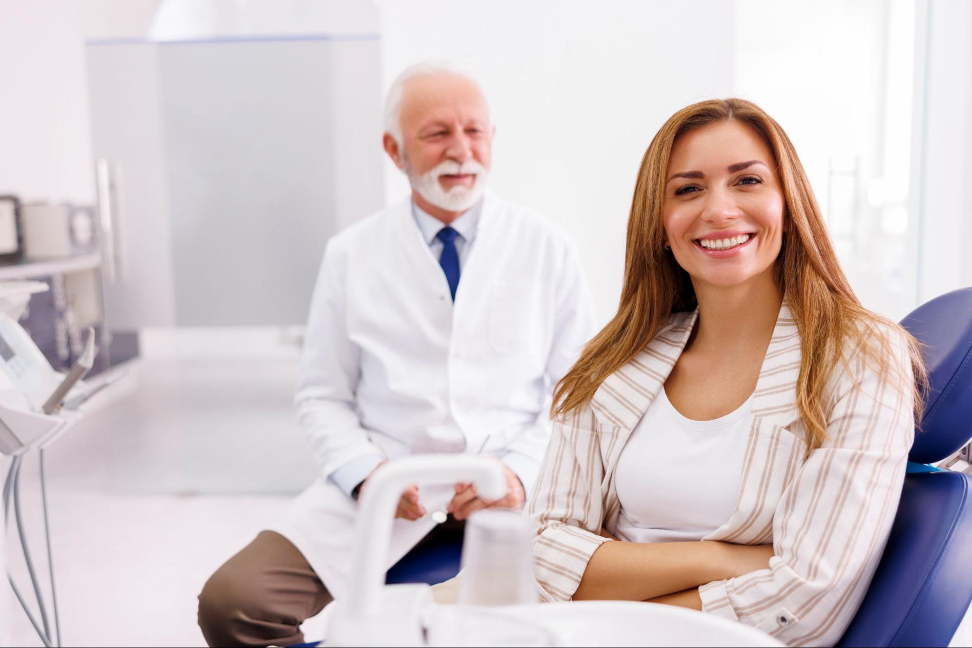 Woman in a dental chair smiling next to a dentist. 