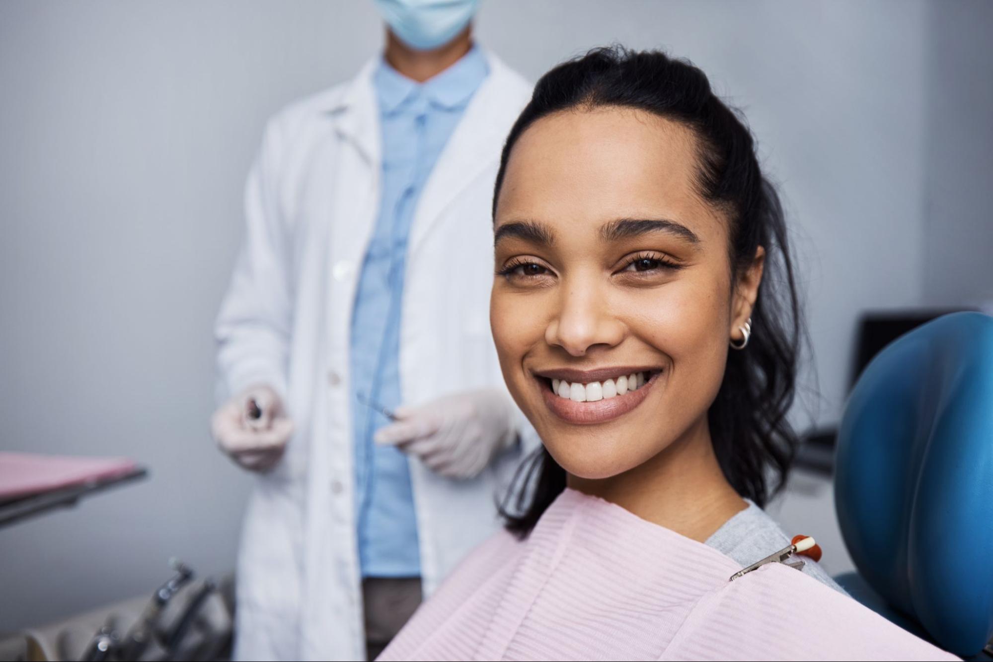 Woman smiling in an exam chair with a dentist in the background.