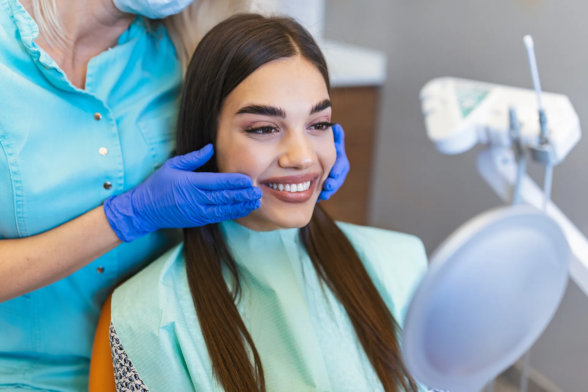 Woman smiling in a dental chair with a dentist adjusting her jaw.
