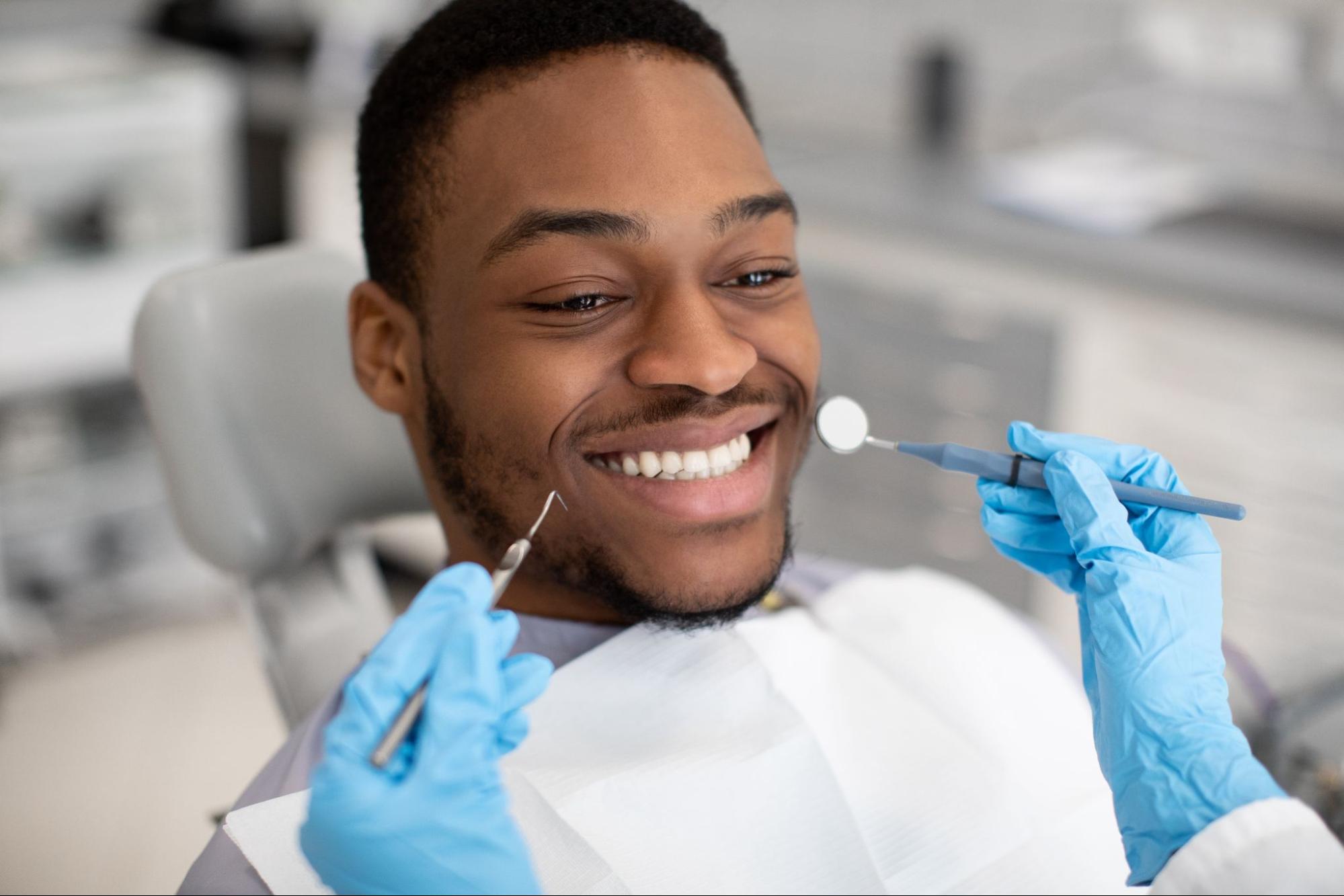 A man smiling with a gloved dentist holding tools beside him.
