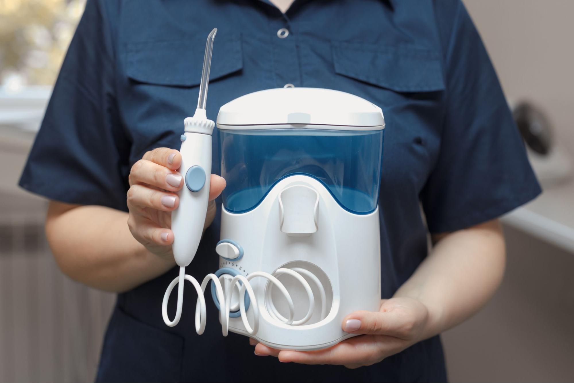A cropped shot of a dentist in a blue top holding a water flosser for dental cleaning and hygiene.