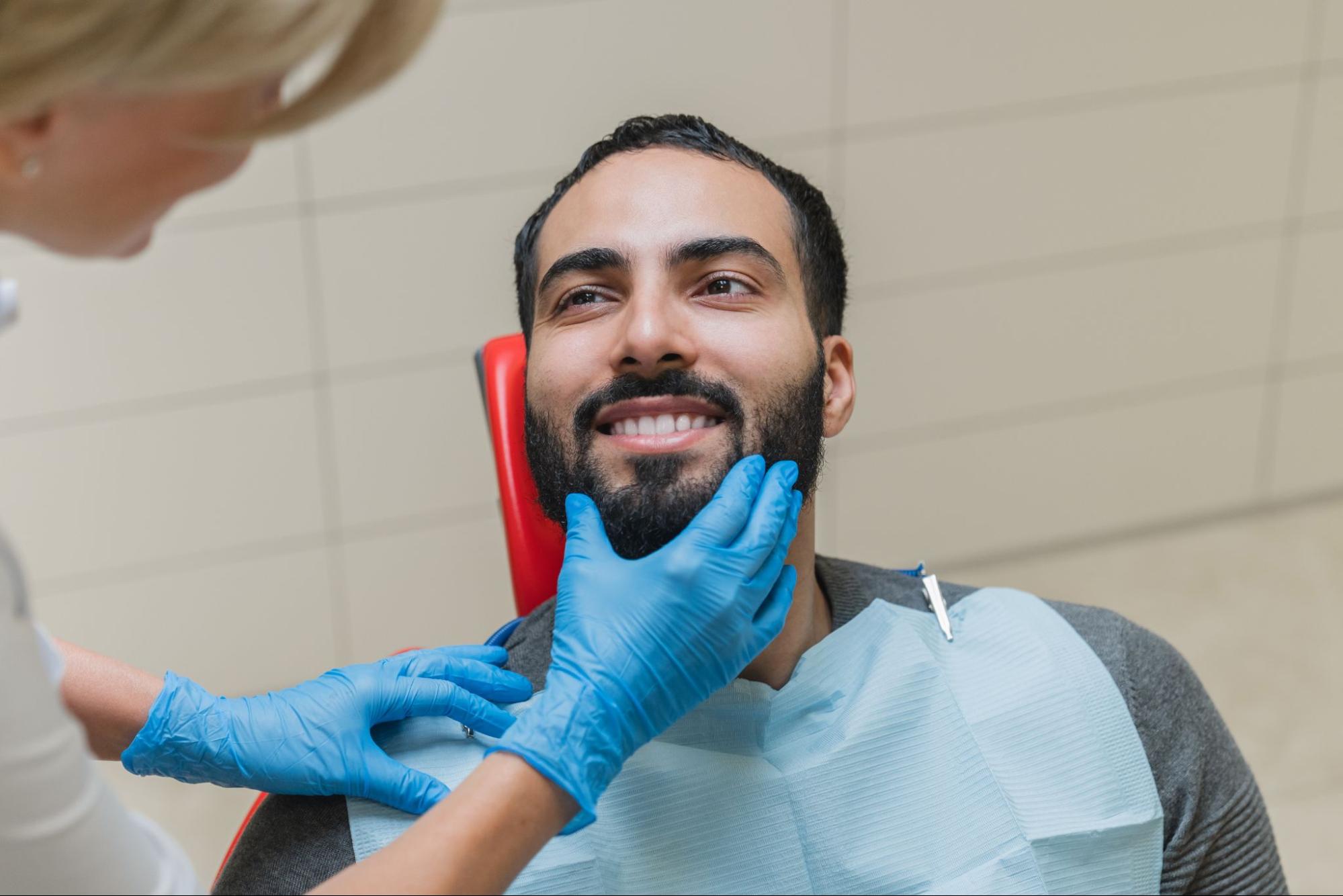 Man smiling in an exam chair with a female dentist wearing gloves holding his chin. 