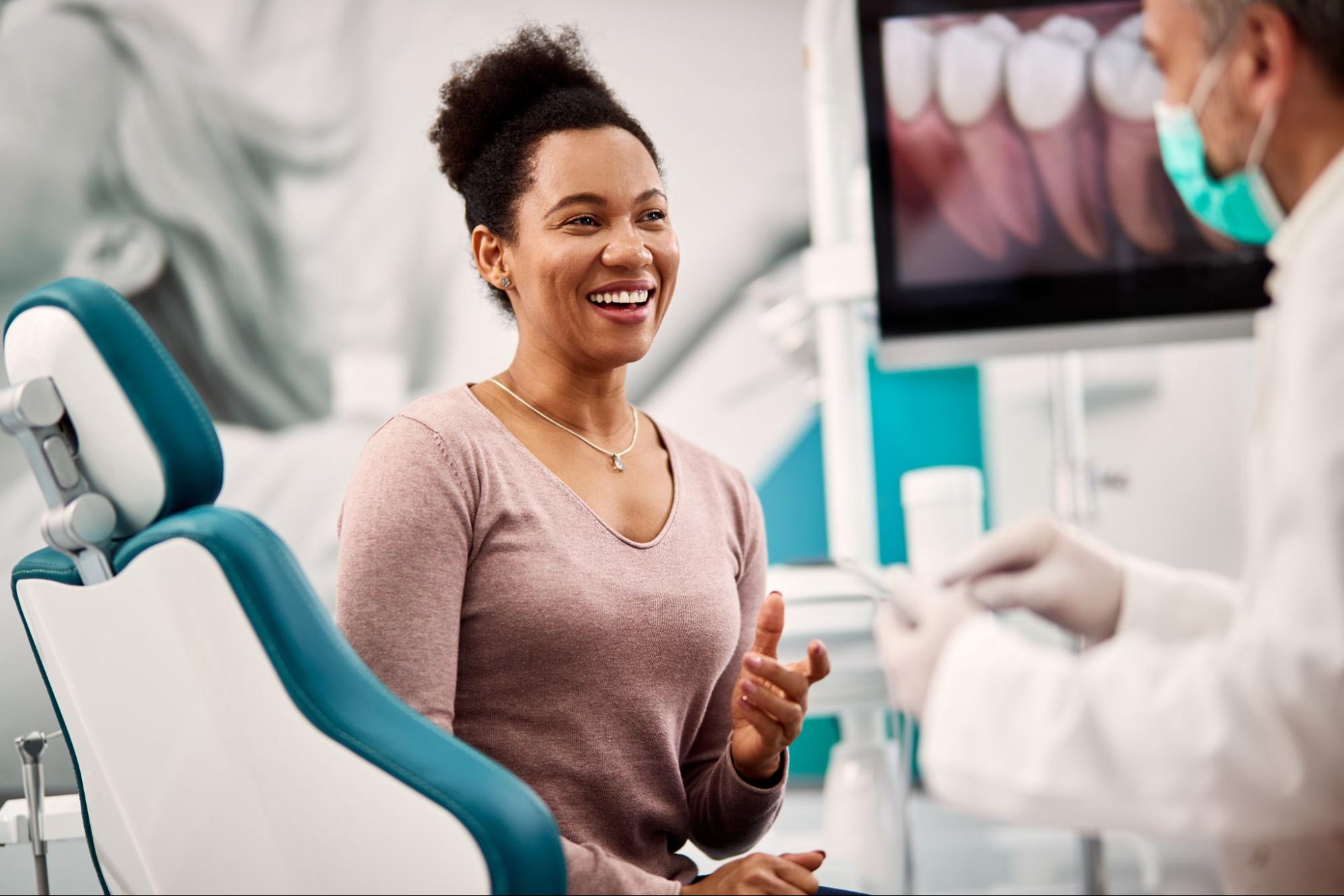 Woman in an exam chair smiling next to a dentist wearing a mask.