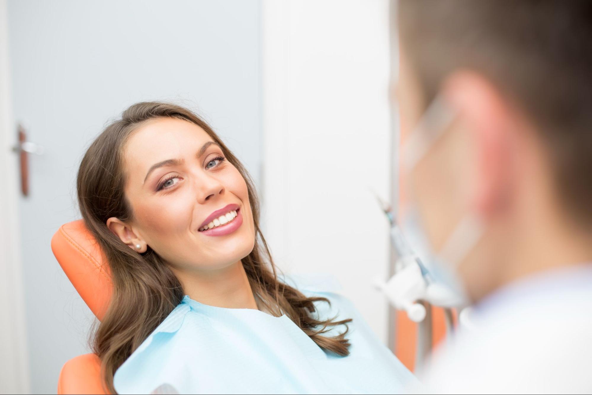Woman smiling and sitting in a dental exam chair next to a dentist. 