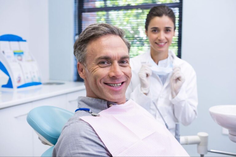 Man smiling in an exam chair next to a dentist.