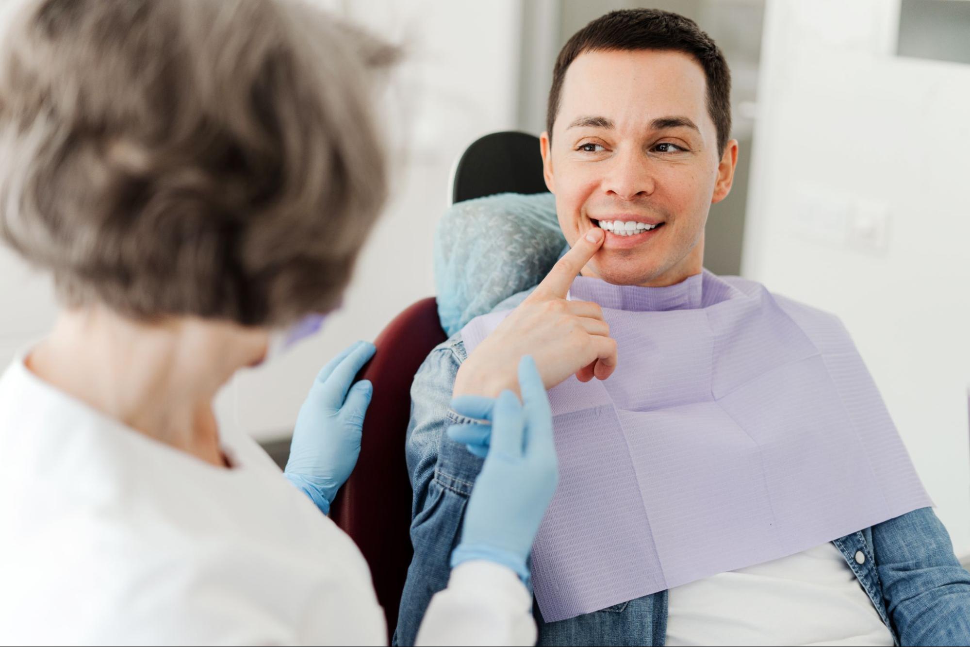 Man smiling and pointing to his tooth next to a female dentist.