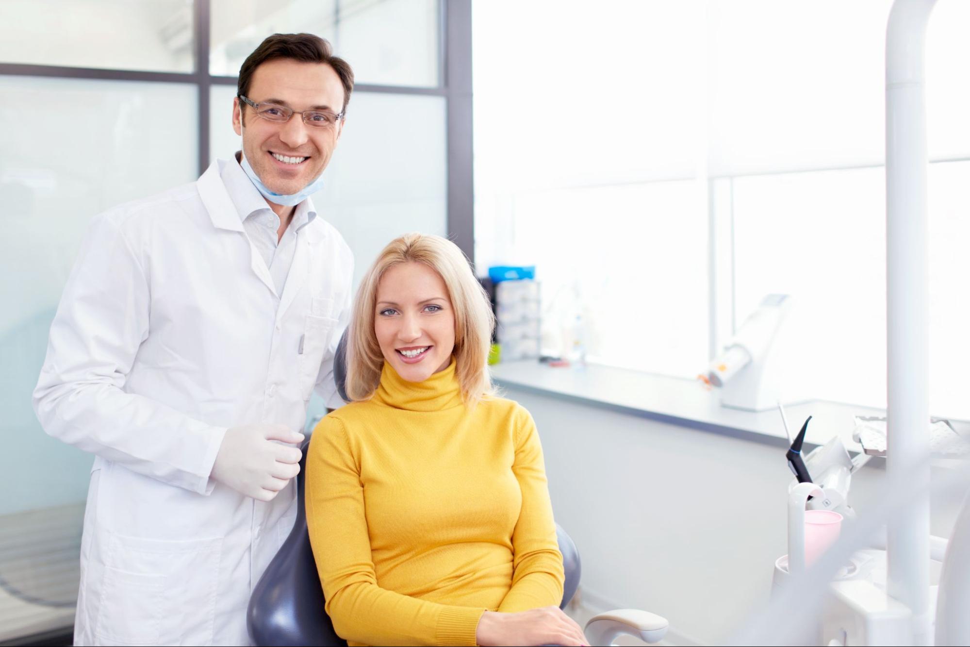 Female patient smiling in an exam chair next to a dentist. 
