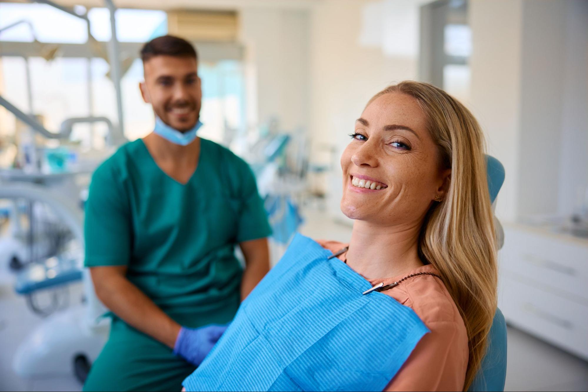 Female patient smiling in an exam chair next to a male dentist. 