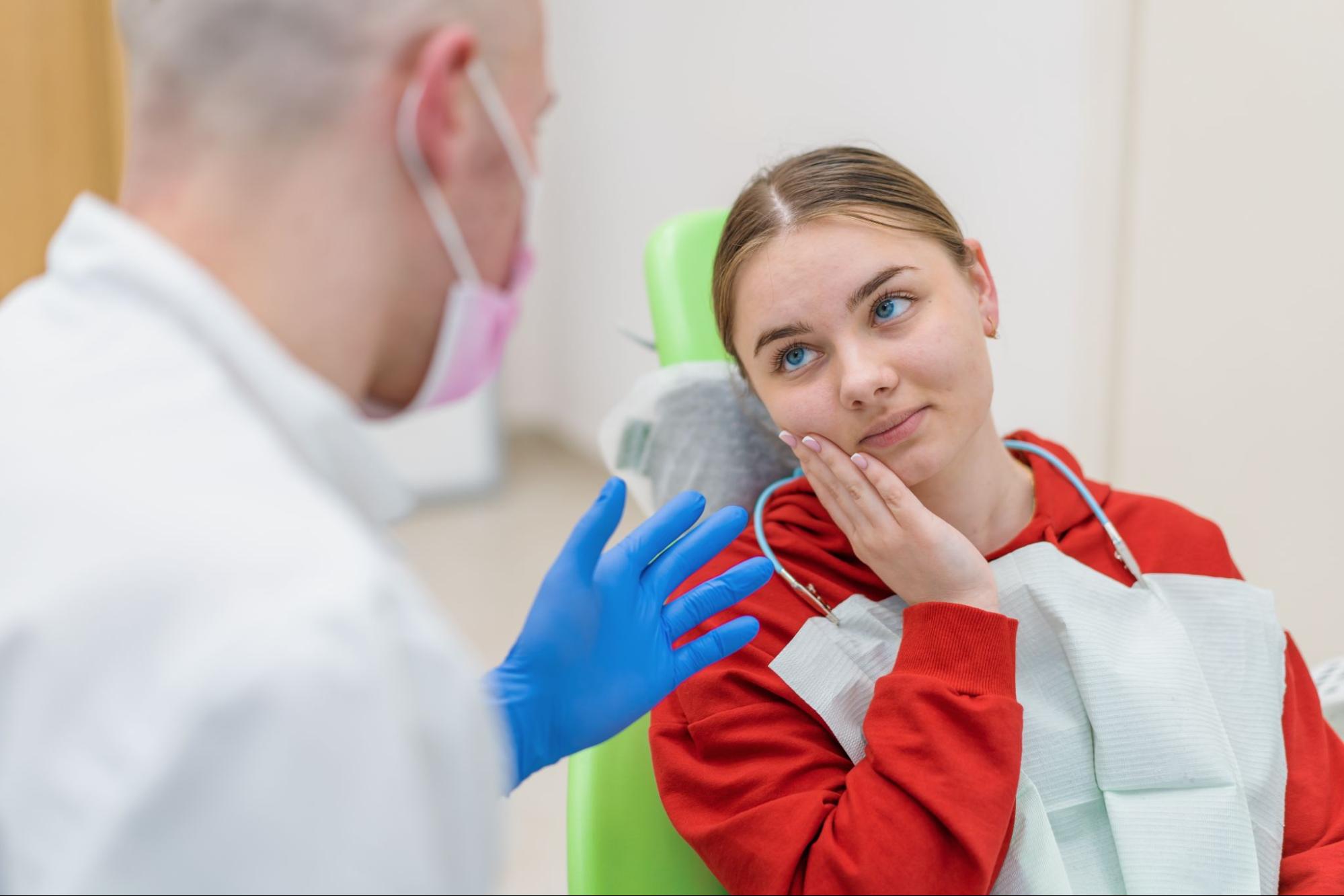 A patient at a dentist's appointment expresses discomfort due to a toothache while the dentist listens and prepares to examine her.