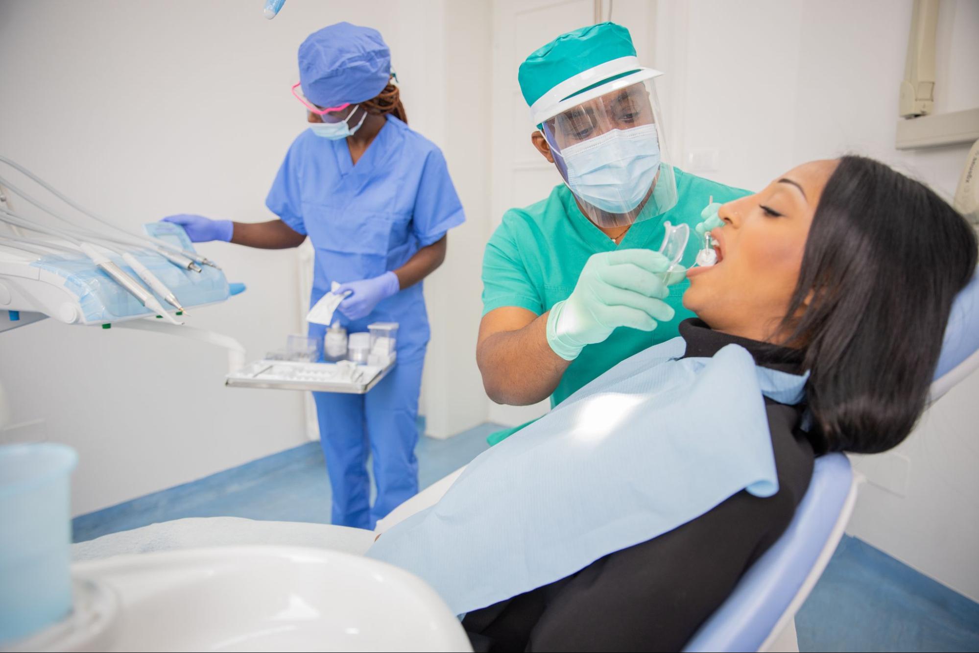 Male and female dental workers next to a woman in an exam chair.