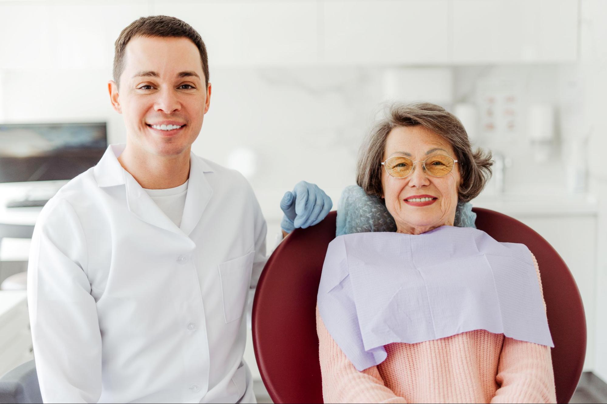 Smiling elderly female patient next to a male dentist. 