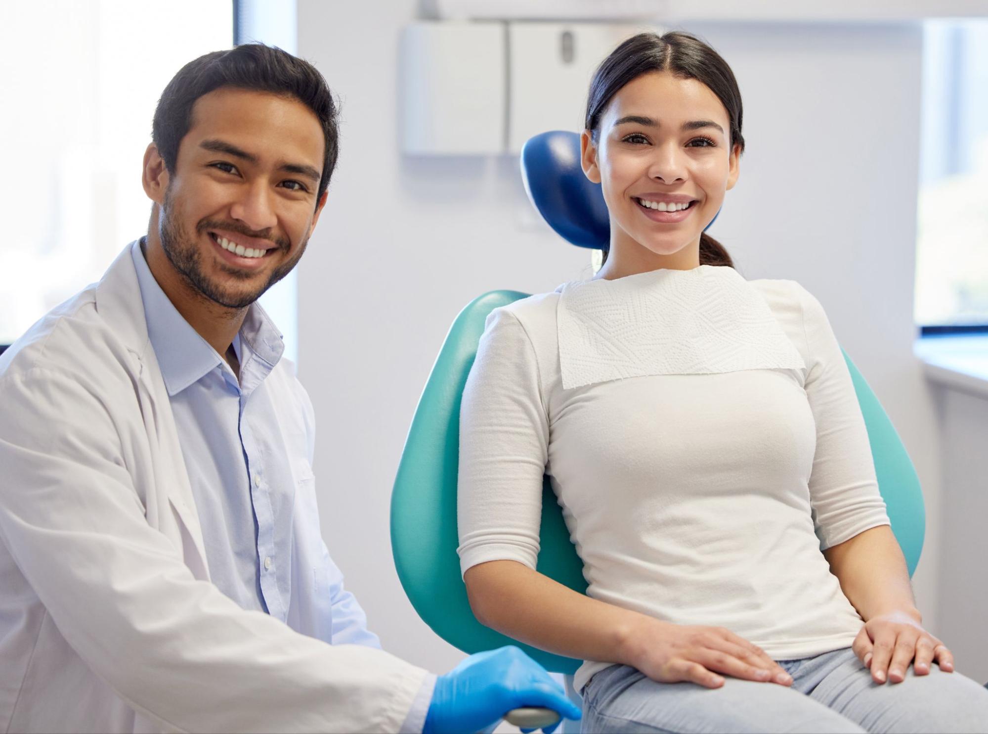 Smiling dentist next to a smiling patient in a chair. 
