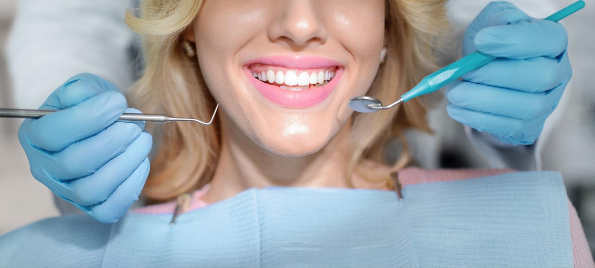 A close-up of a female patient's smile after a gum contouring procedure, with the dentist's hands holding tools.