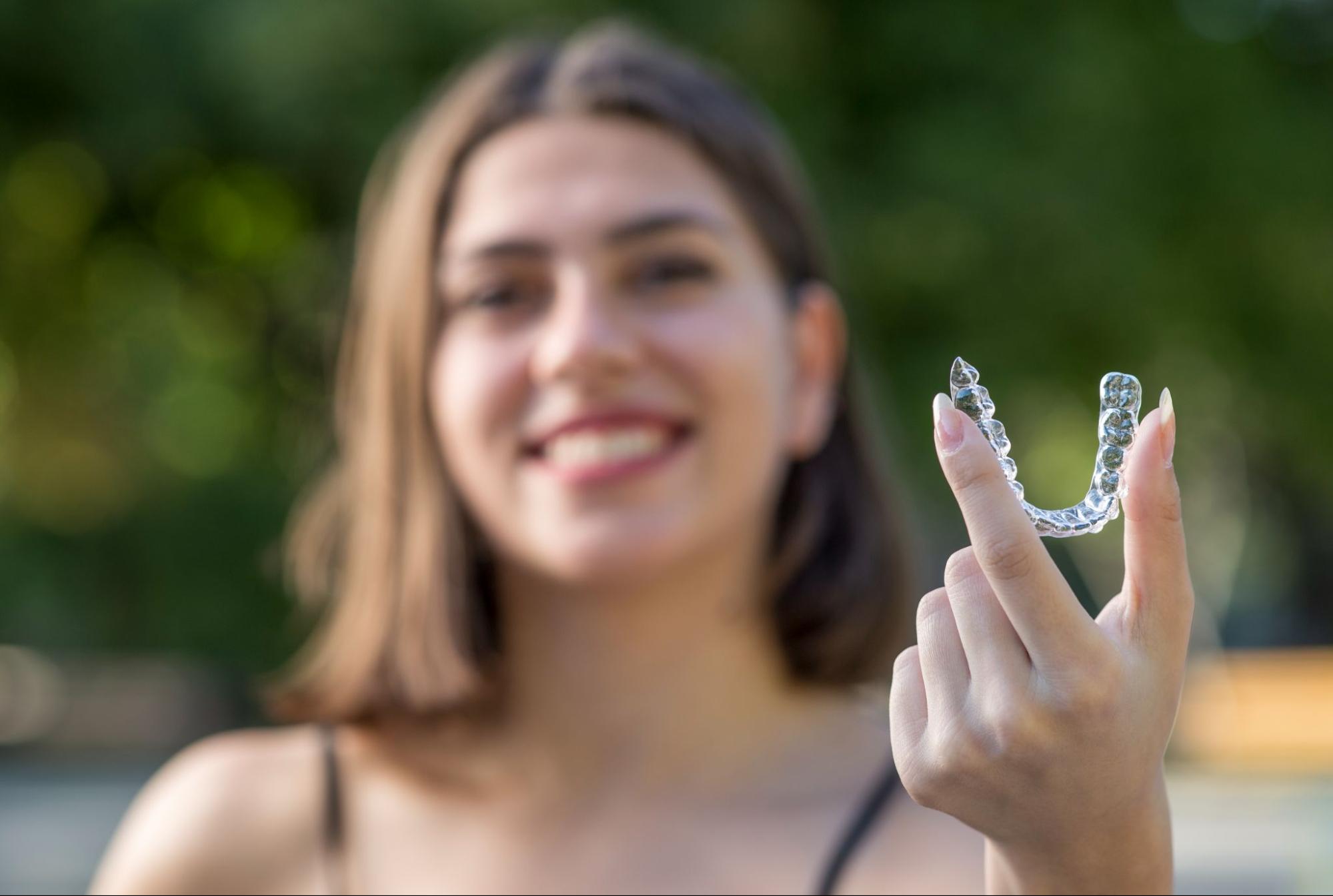 Woman smiling and holding a clear aligner.