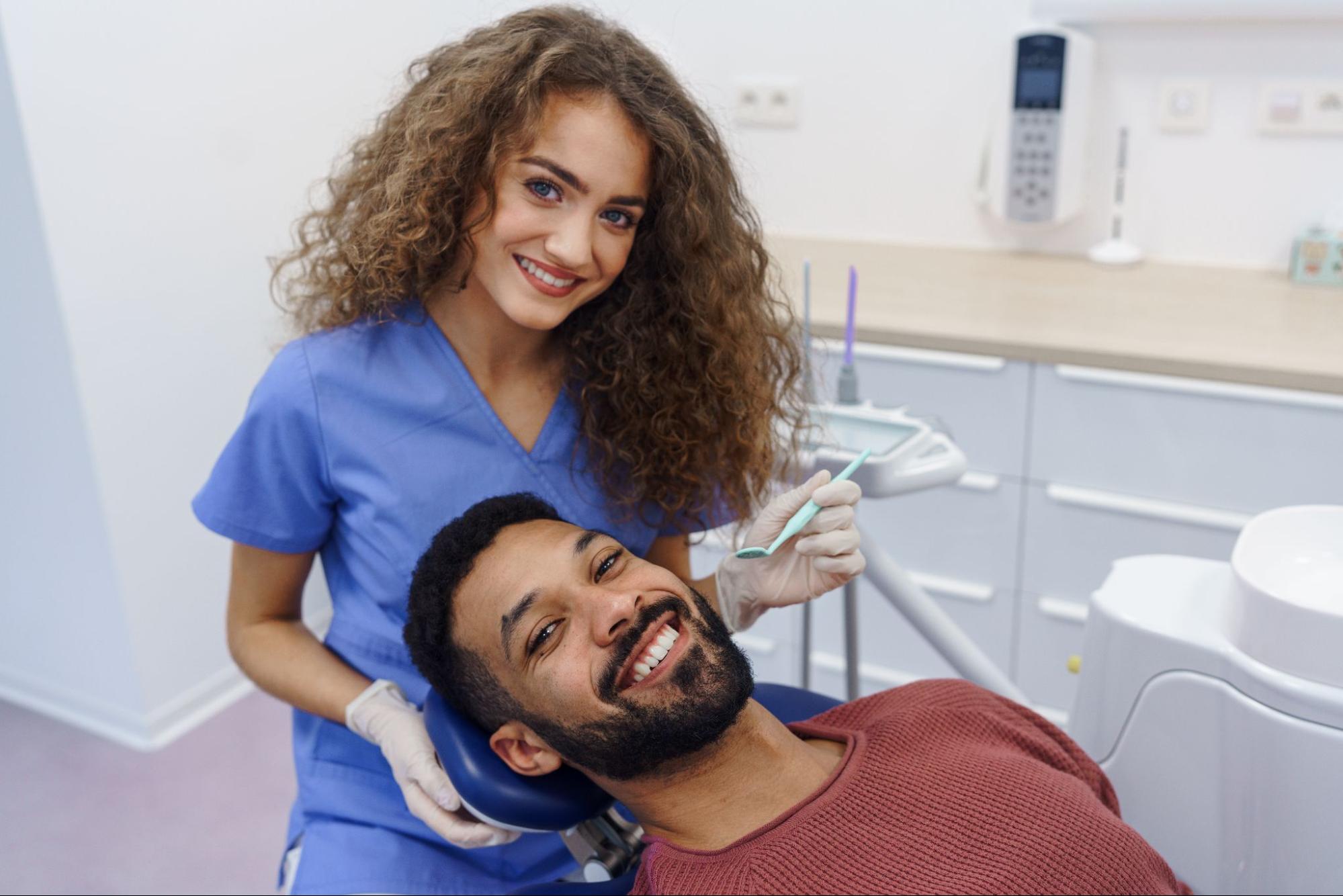 Female hygienist using a dental tool on a man in an exam chair who is smiling. 