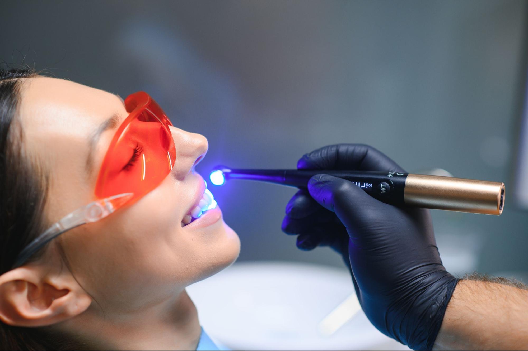 A young woman undergoes a dental filling procedure with a UV curing light at a dental clinic.