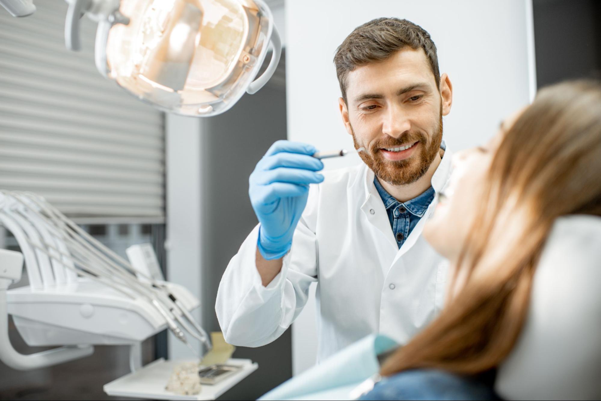 A male dentist prepares to insert a dental tool into a patient's mouth to examine her dental condition during a routine checkup.