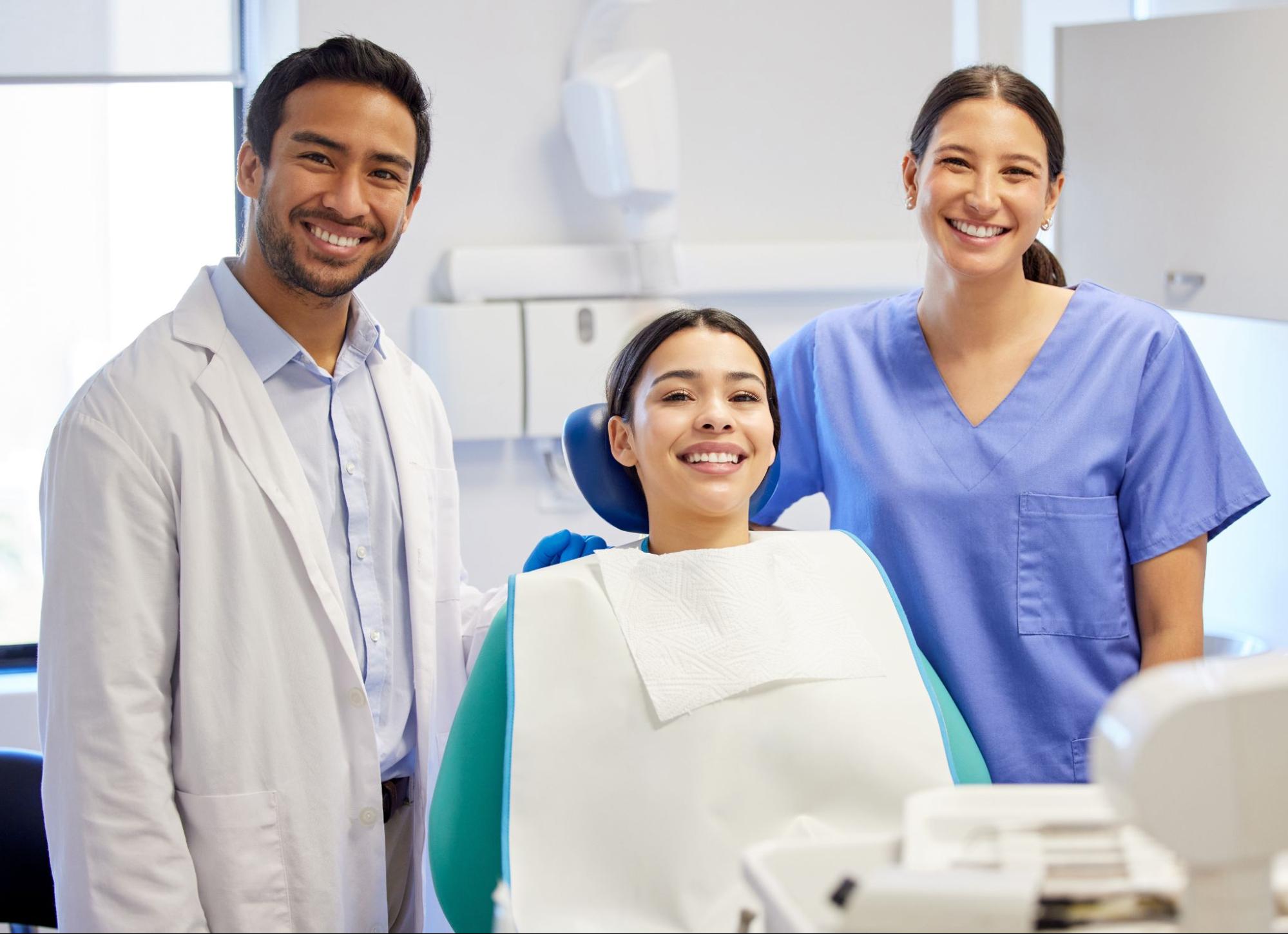 Woman in an exam chair smiling next to two dental professionals. 
