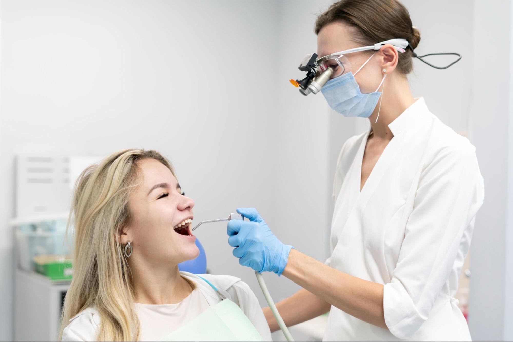 A female dentist uses a water and air syringe tool during a dental treatment on a female patient in a clinic.