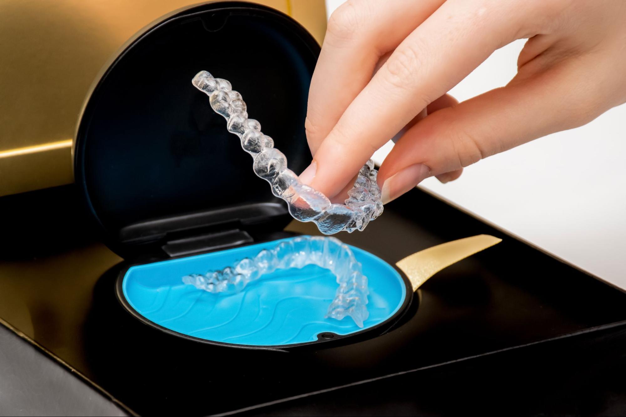 A lady’s hand places clear Invisalign® aligners into a blue and black protective case.
