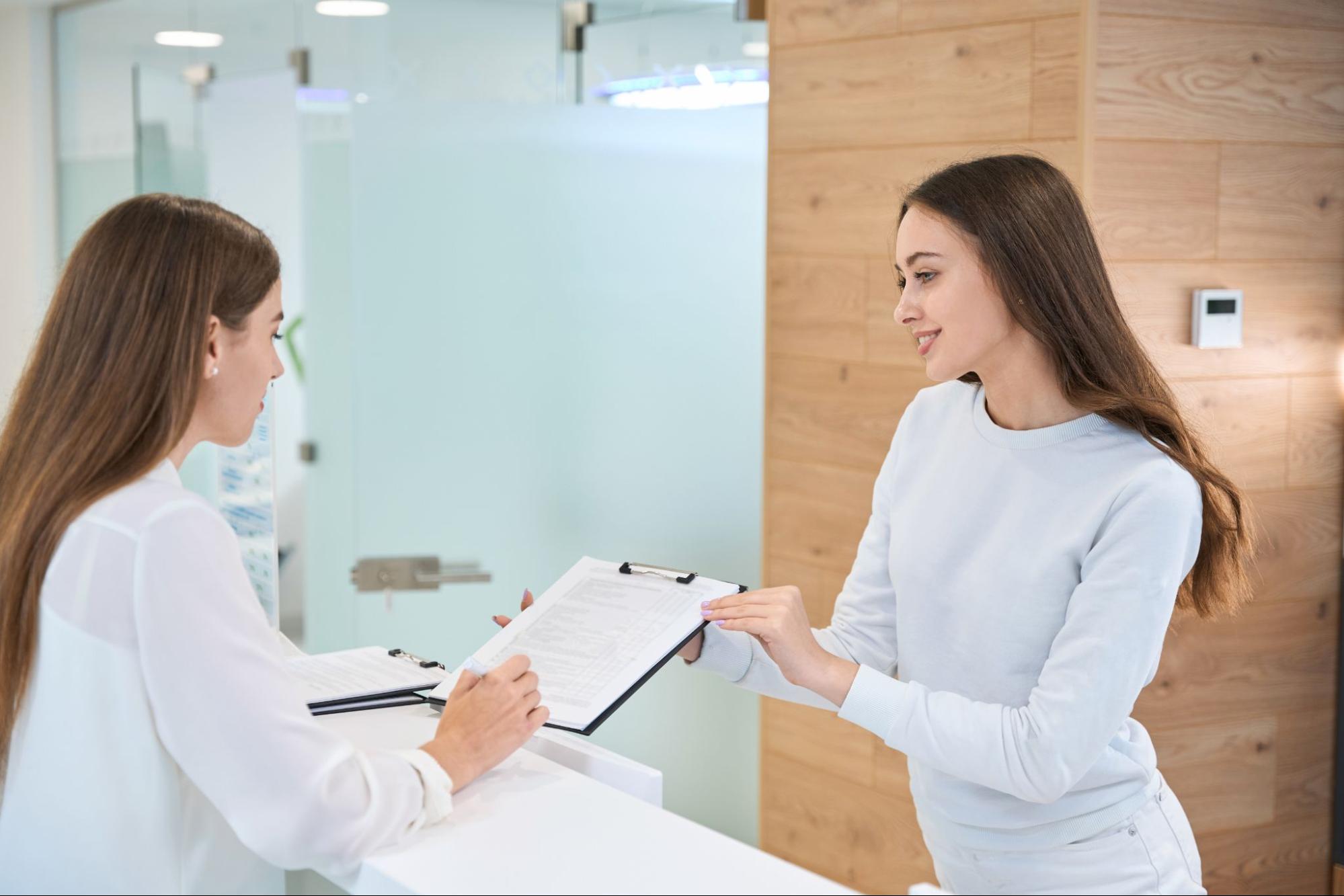 Woman speaking to a female secretary at a dentist office.