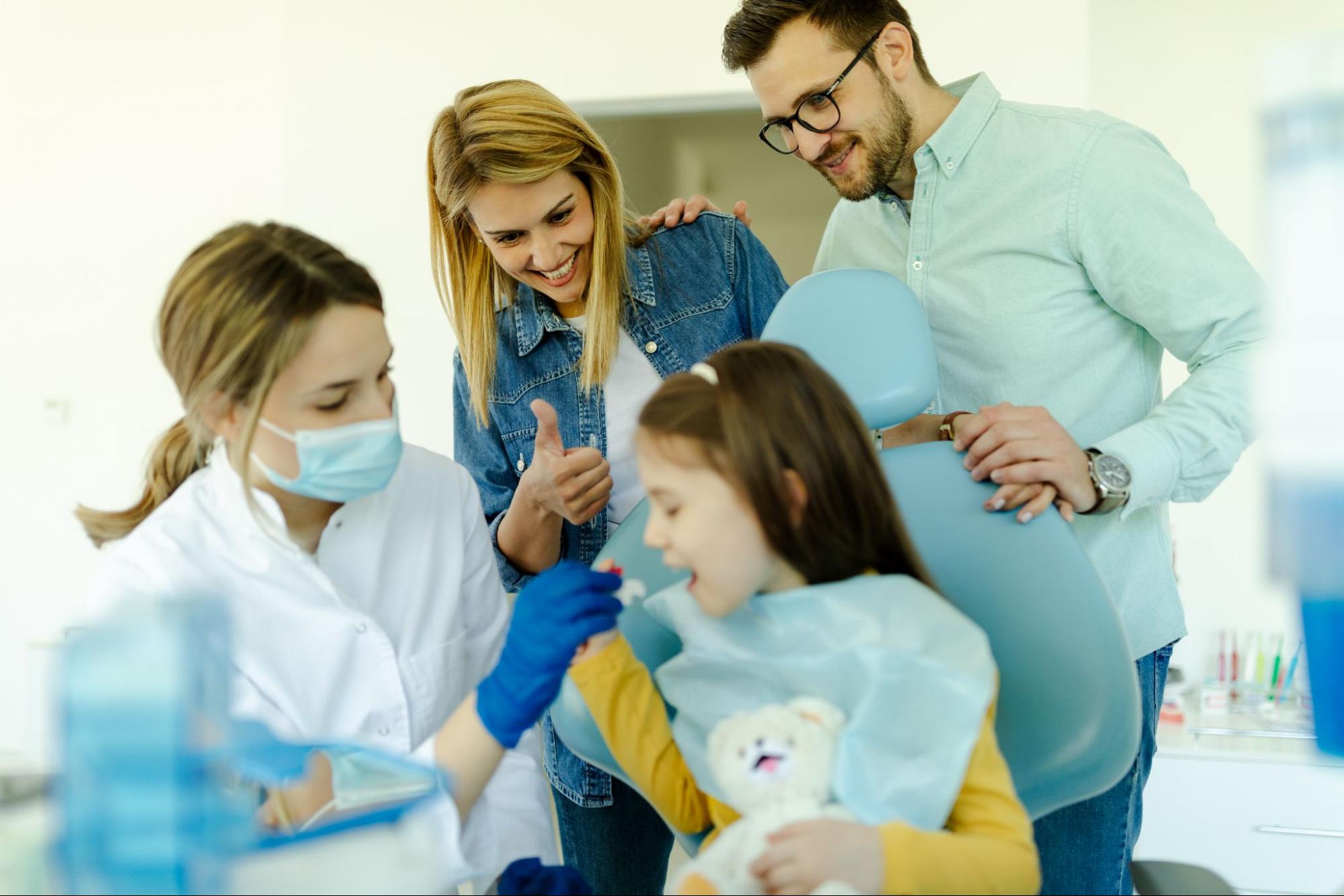 Young girl in a dental exam chair next to her parents.