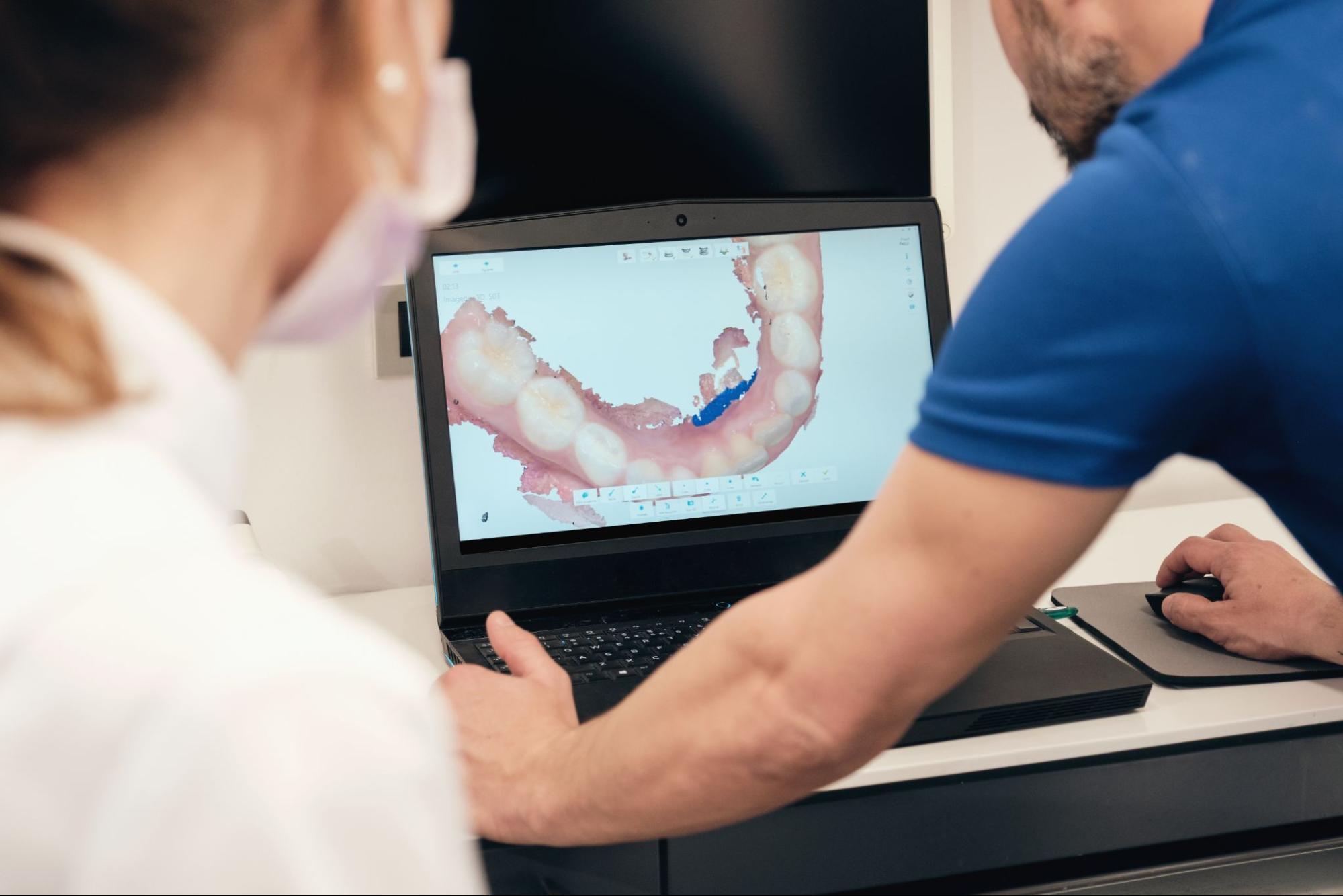 A male dentist reviews a teeth scan with a colleague while discussing a dental bridge procedure.