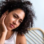 A woman touches her ear in pain, showing signs of TMJ.