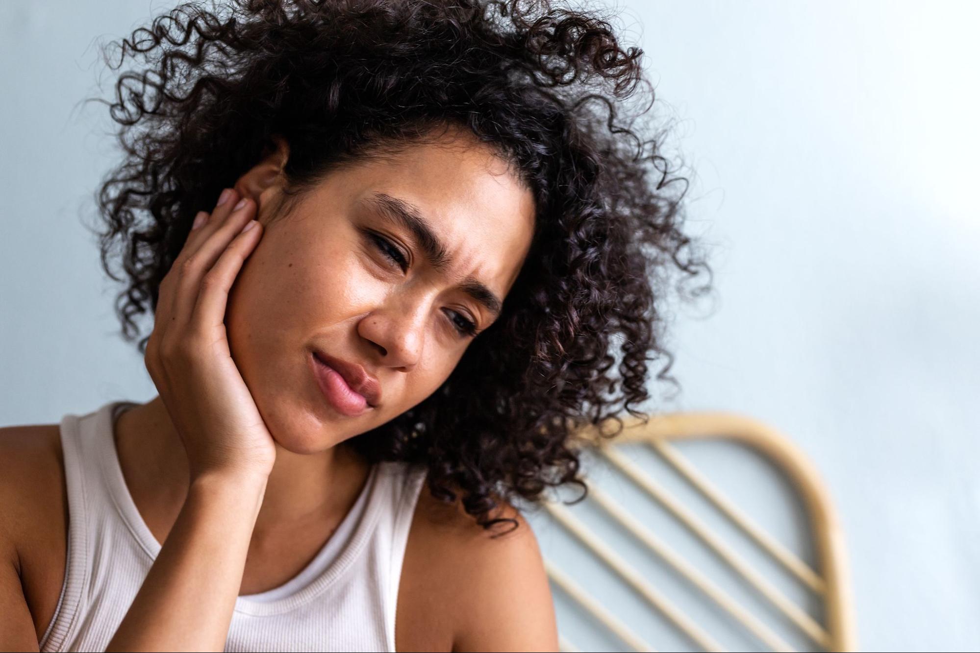 A woman touches her ear in pain, showing signs of TMJ.