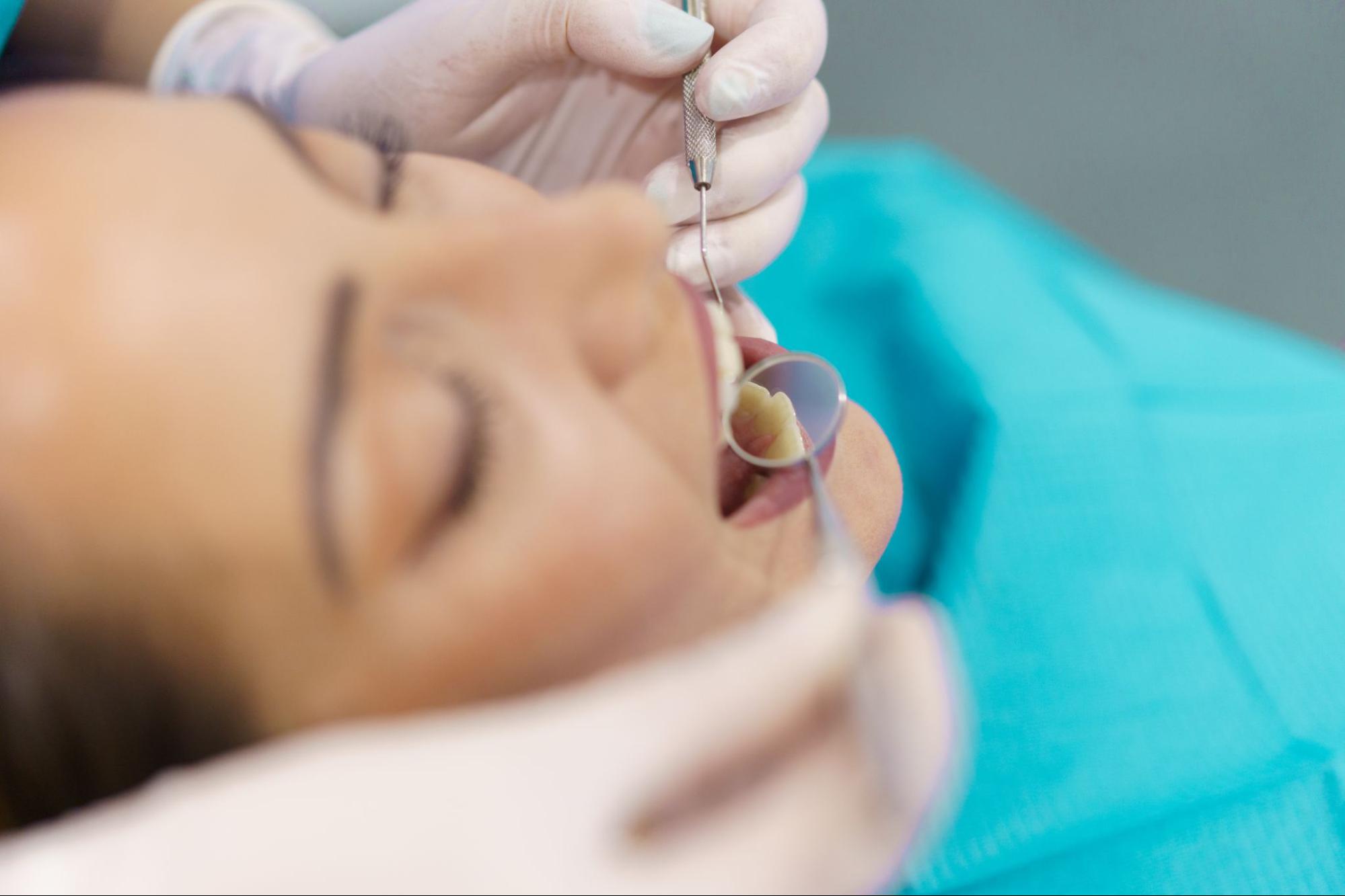 A dentist examines a patient’s mouth with a dental mirror.