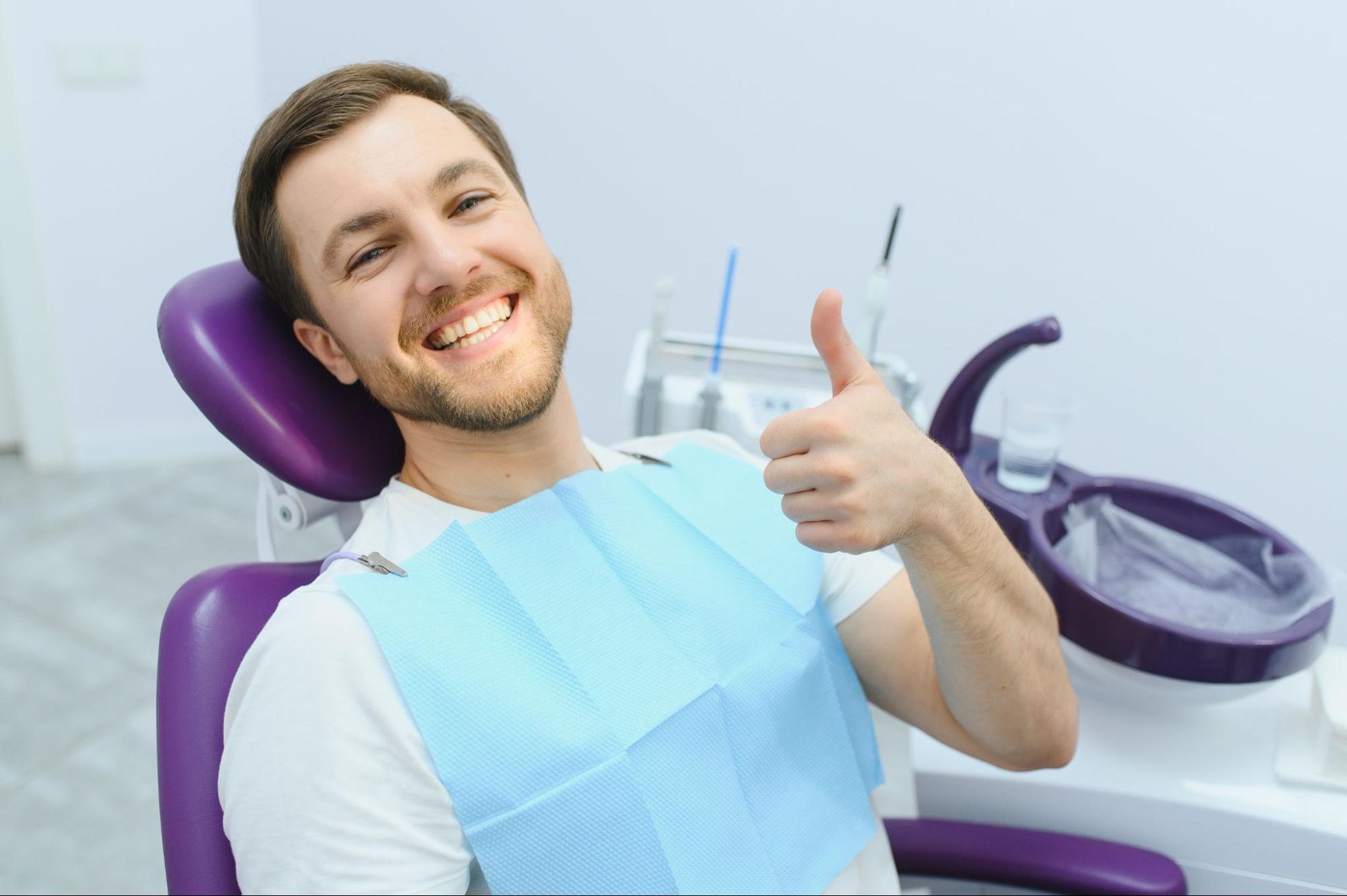 Smiling man at dentist's office giving thumbs up post-treatment.