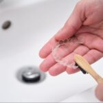 A close-up of cleaning retainers with a bamboo toothbrush to remove organic residue from clear aligners.