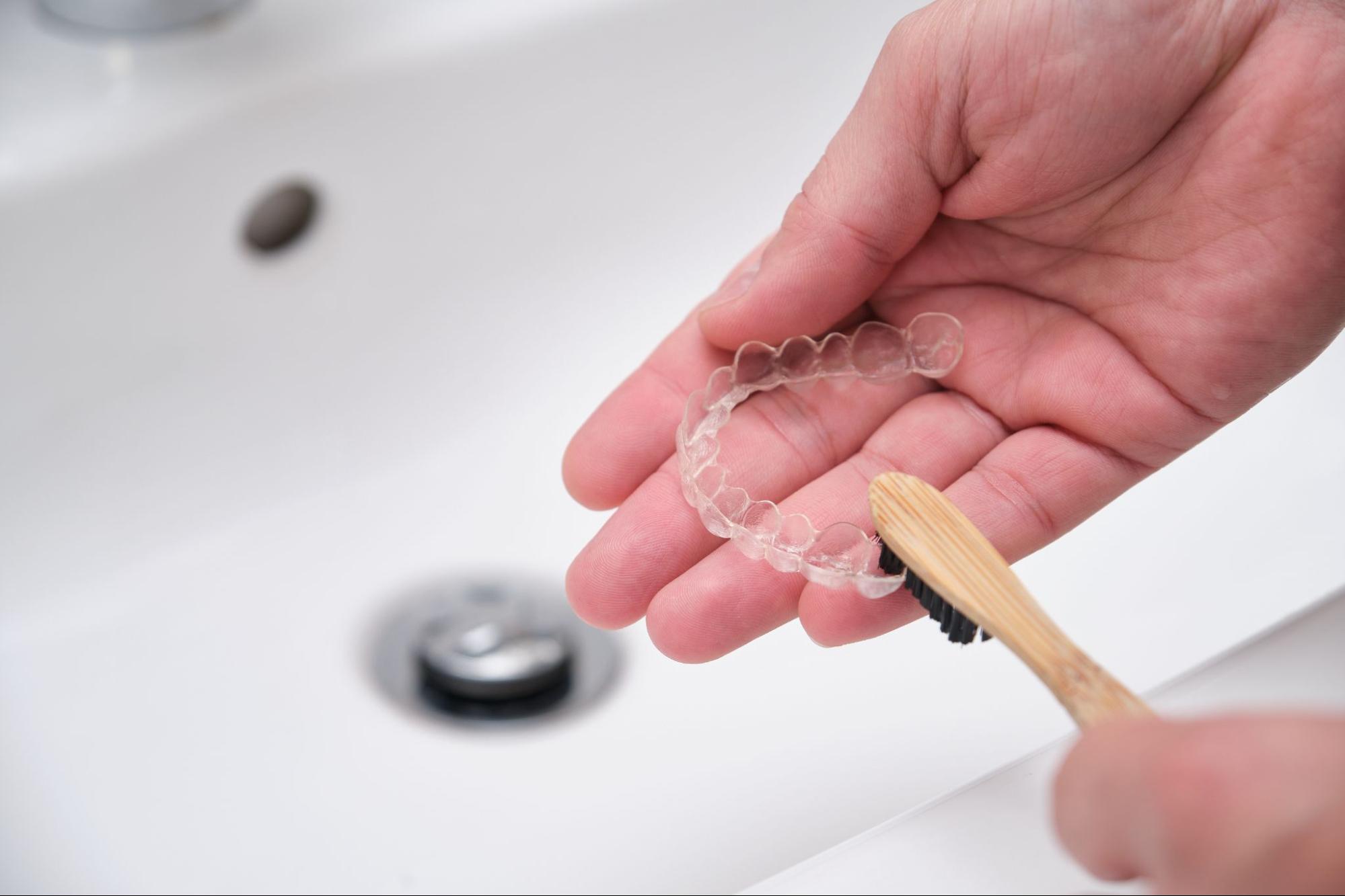 A close-up of cleaning retainers with a bamboo toothbrush to remove organic residue from clear aligners.