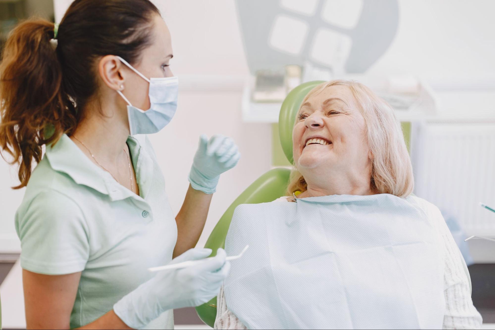 Elderly woman smiling in an exam chair next to a female professional.