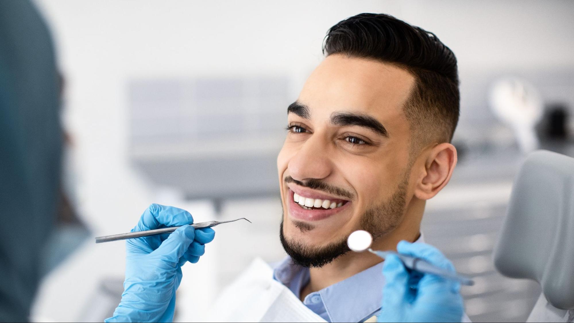 Man smiling in a dental exam chair next to a dentist holding tools. 