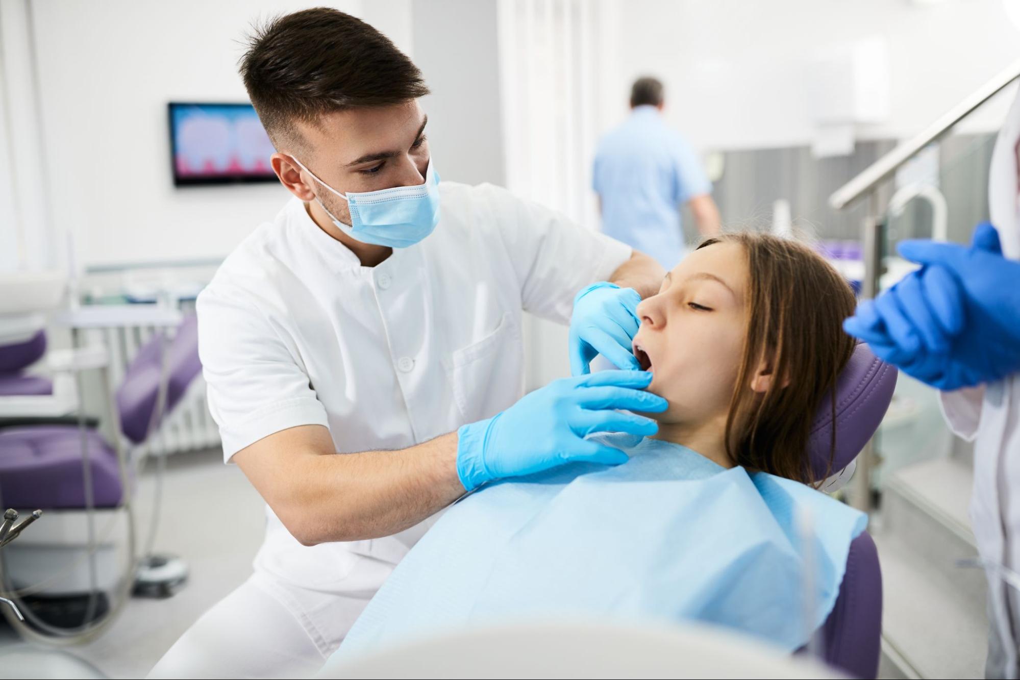 A male dentist performing a routine teeth check on a female teenage patient.