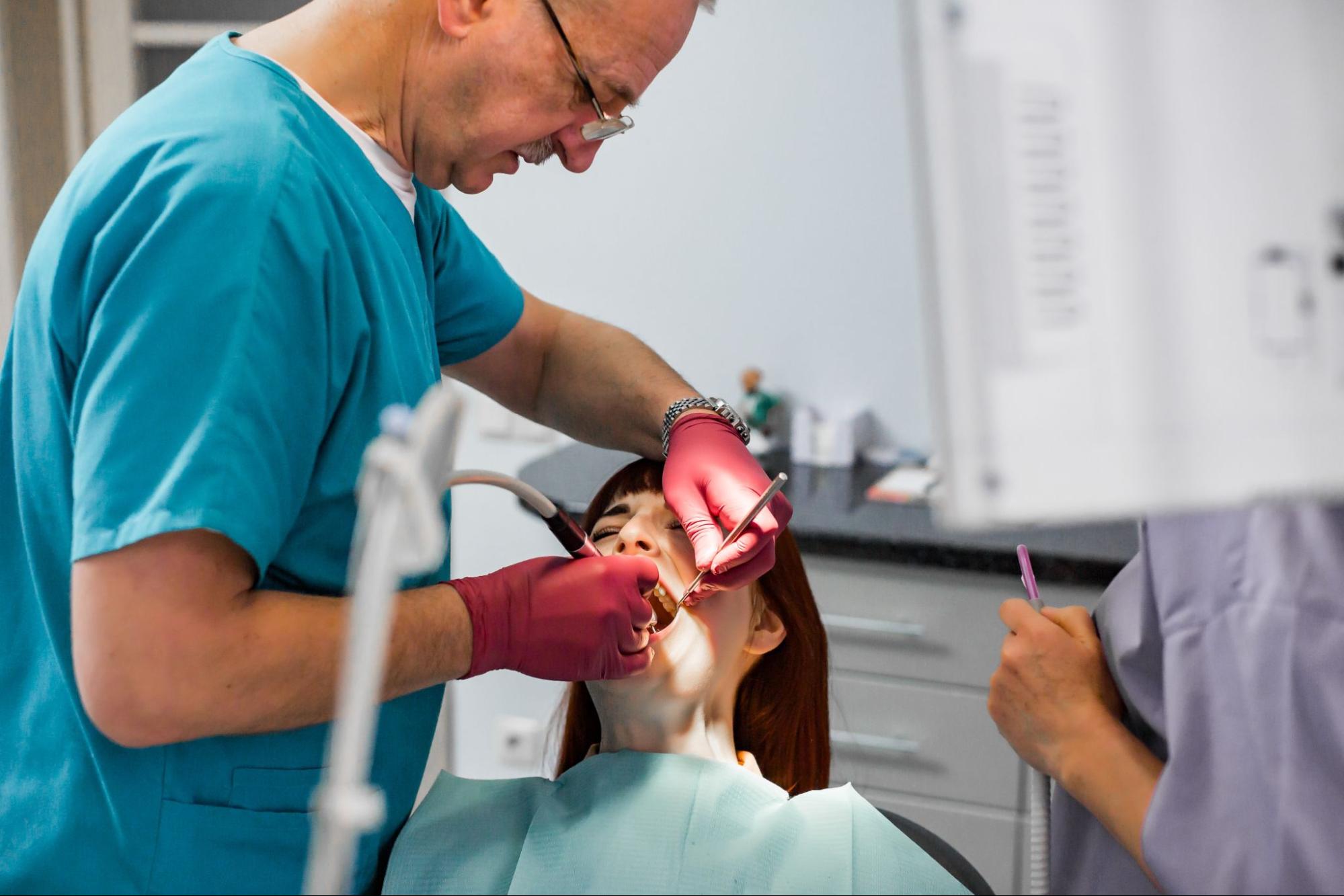 A senior male dentist and assistant perform treatment for periodontitis on a patient.