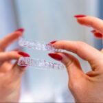 Close-up of a woman’s hands holding clear Invisalign® retainers.