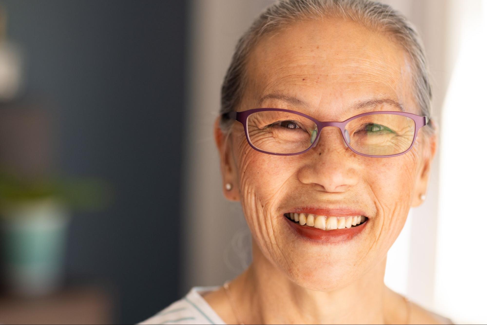 Older woman in glasses smiling with white teeth. 
