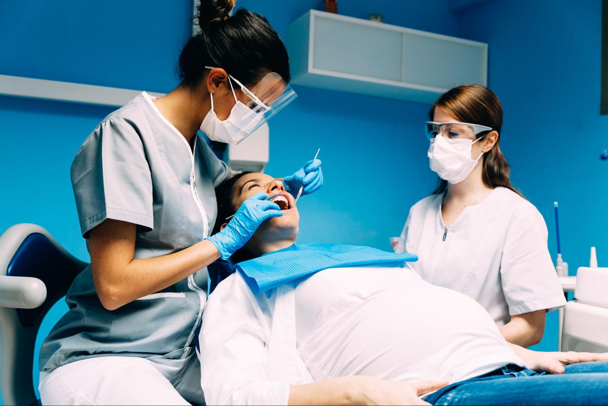 A female dentist treats a patient for gum disease while the assistant observes during the procedure.