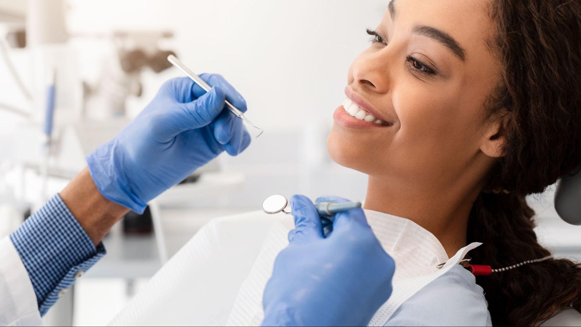Woman smiling with a dentist holding tools. 