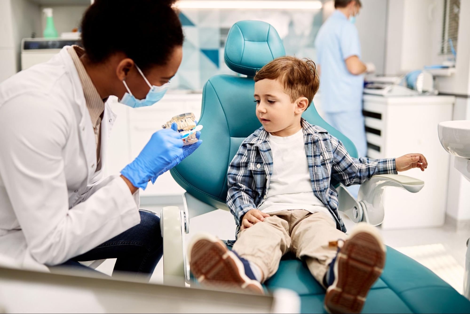 Young boy in a dental exam chair speaking to a dentist.