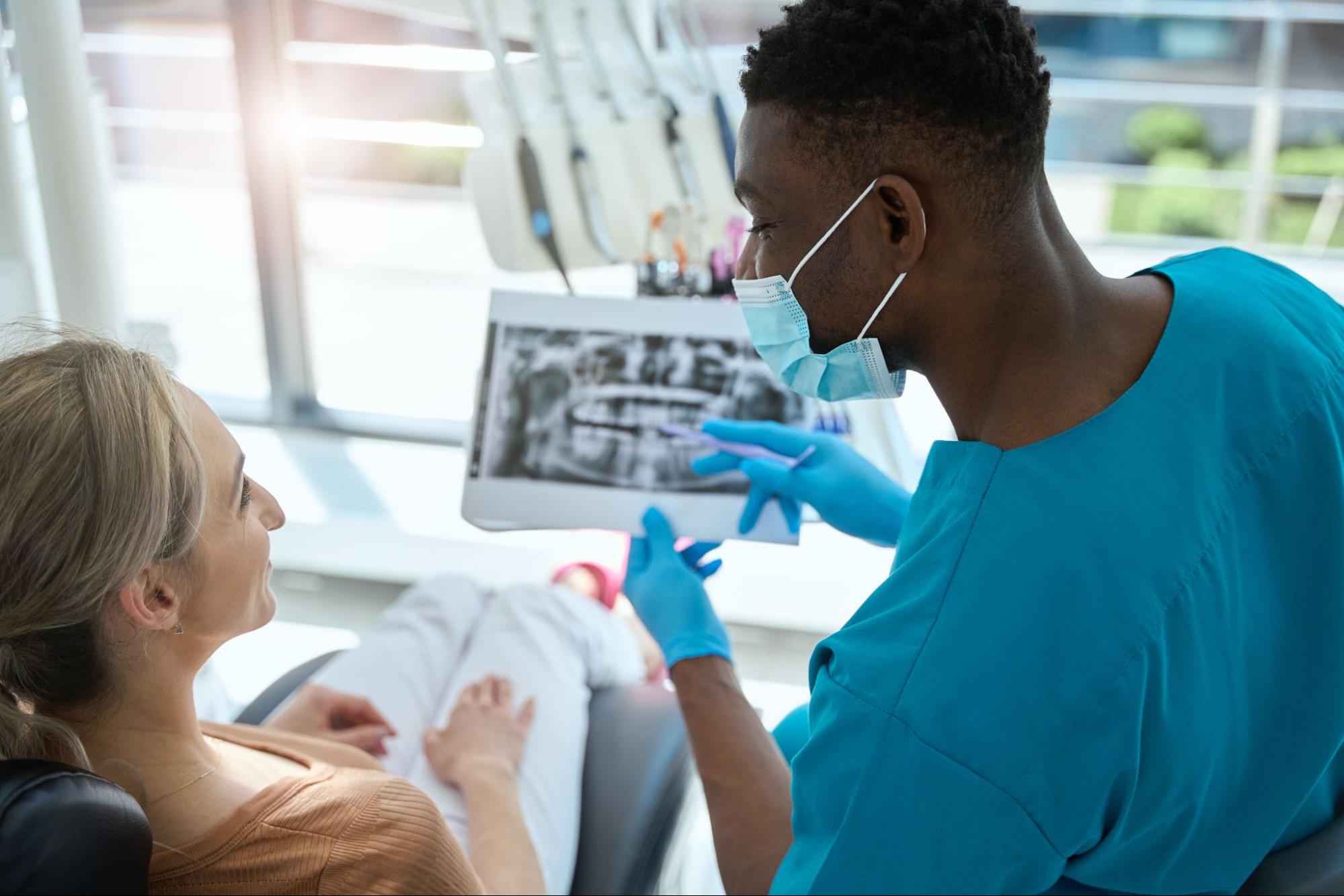 A male dentist shows and explains the X-ray results to a female patient. 