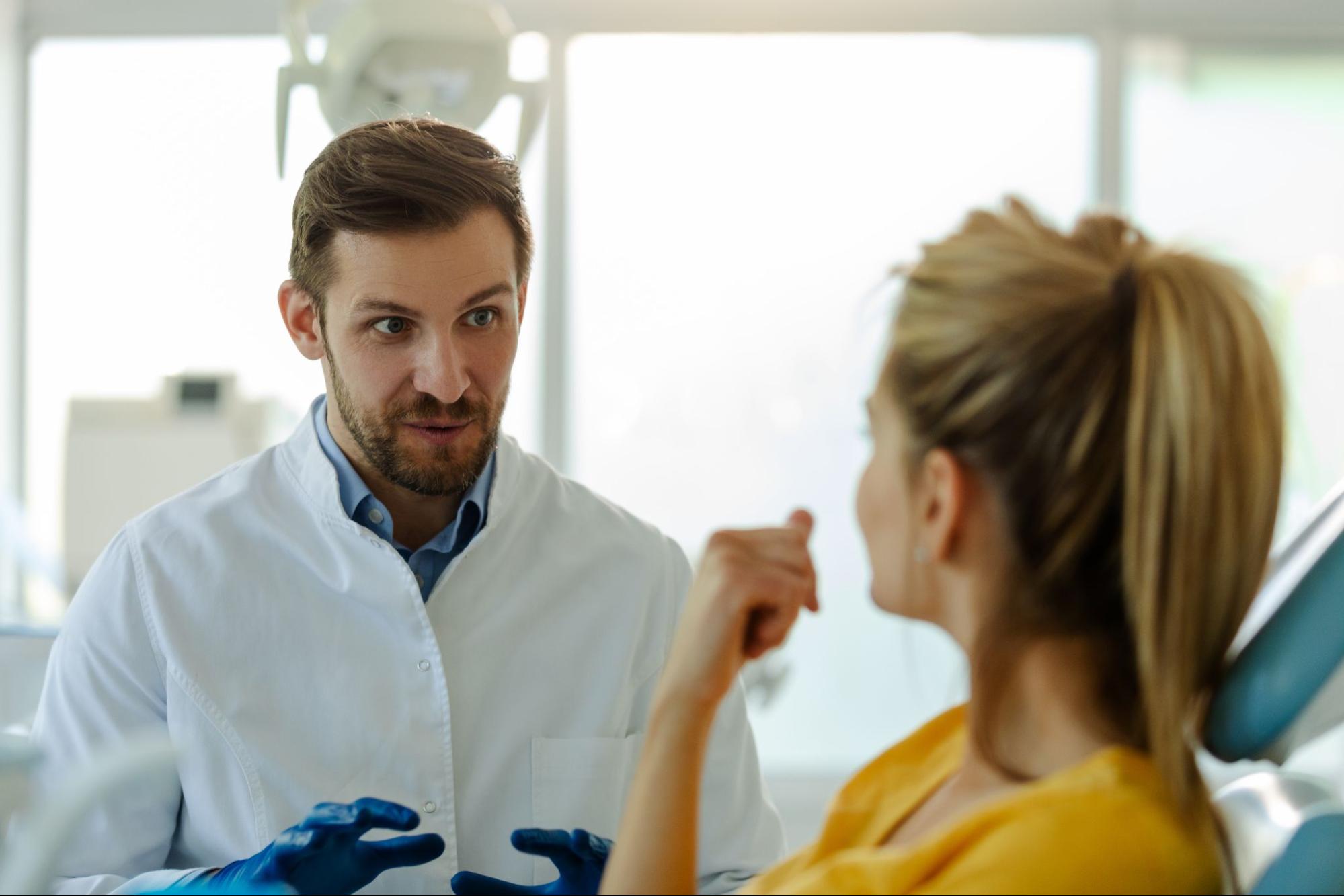 Male dentist speaking to a female patient in an exam chair. 