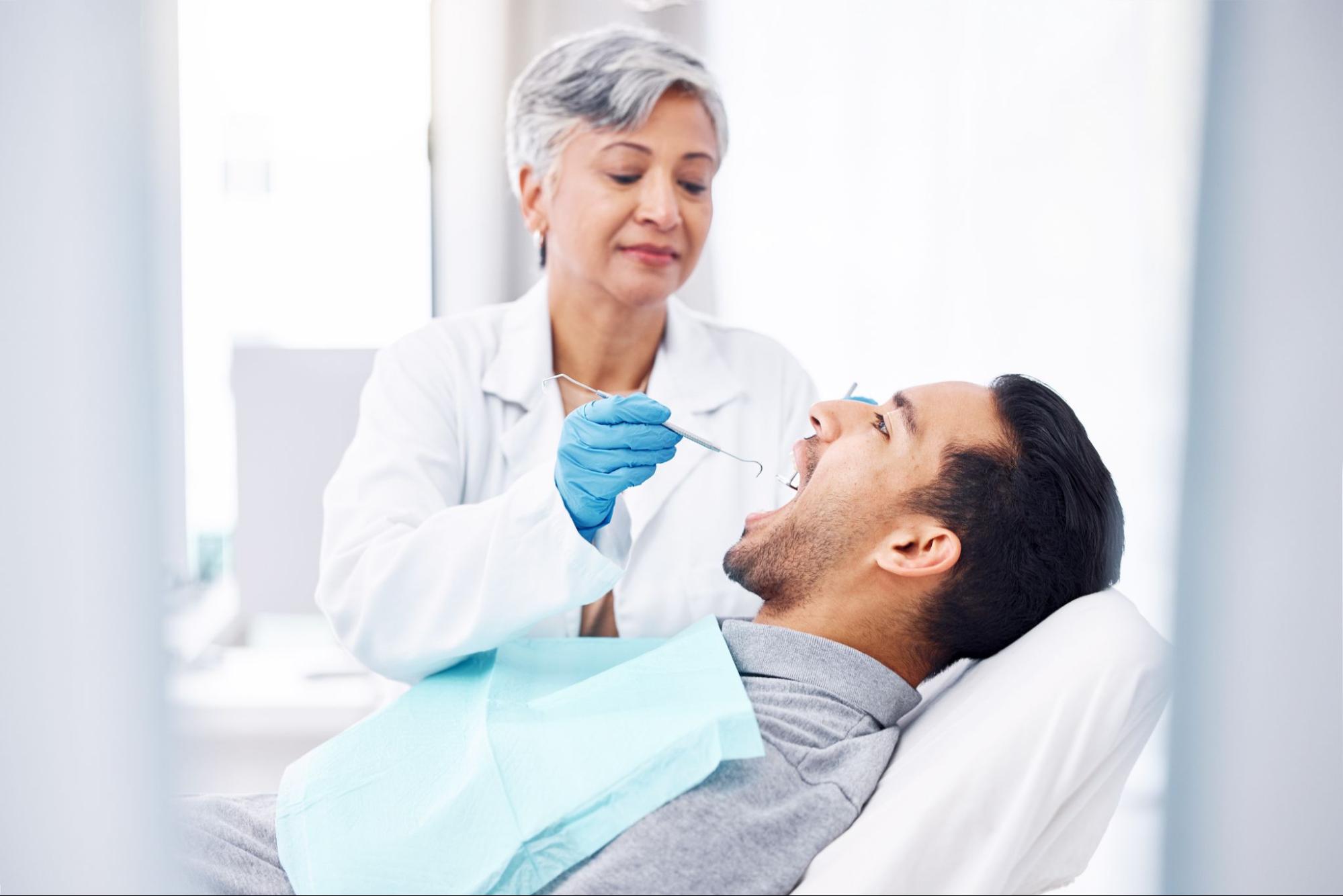A woman dentist examines a man's teeth using dental tools during a gum disease treatment, ensuring oral health and proper care for a healthier smile.