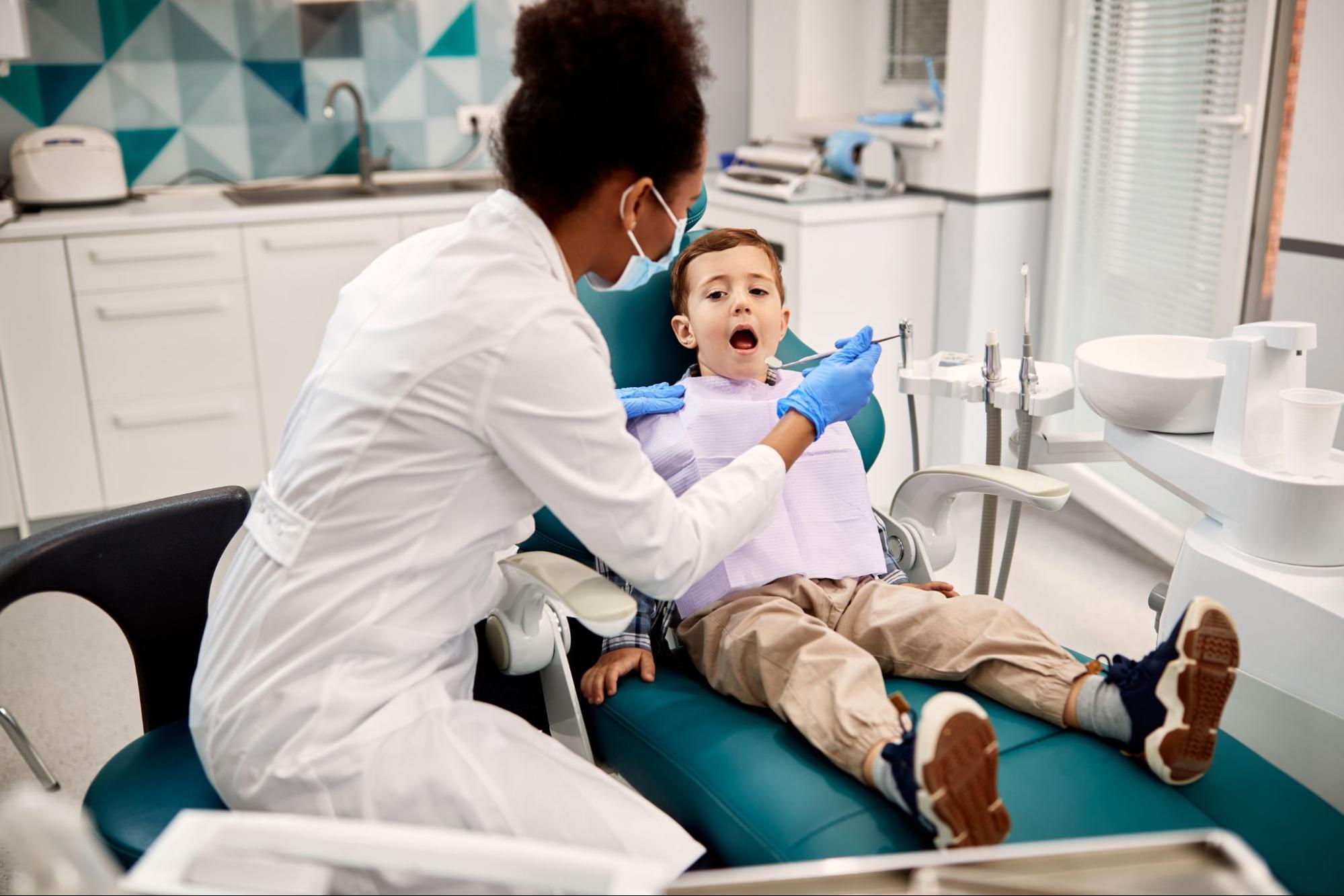 A black female pediatric dentist examines a young boy’s teeth during a routine checkup at the dental office, creating a calm and caring environment.