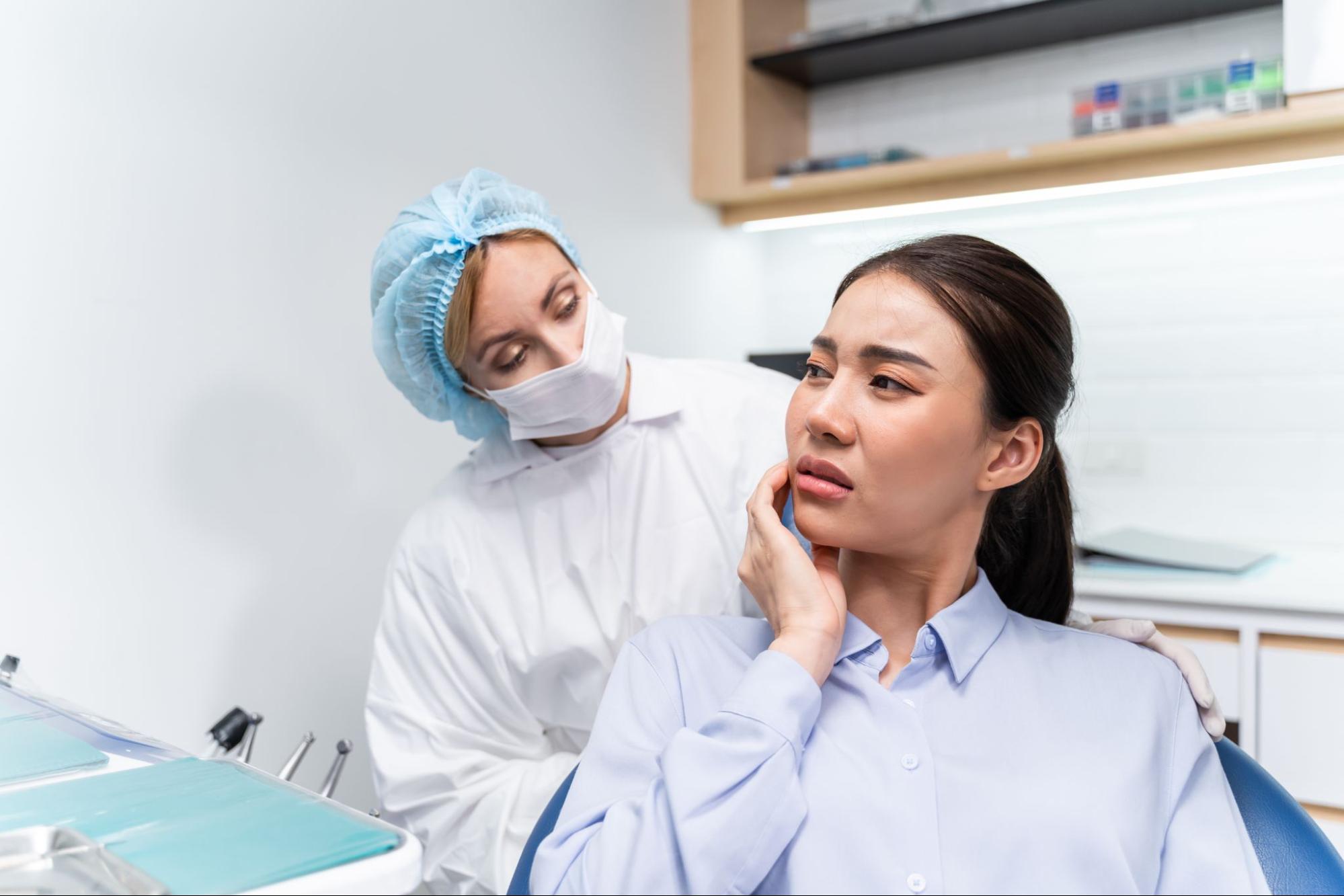 A dentist in cap and mask examines a young girl.