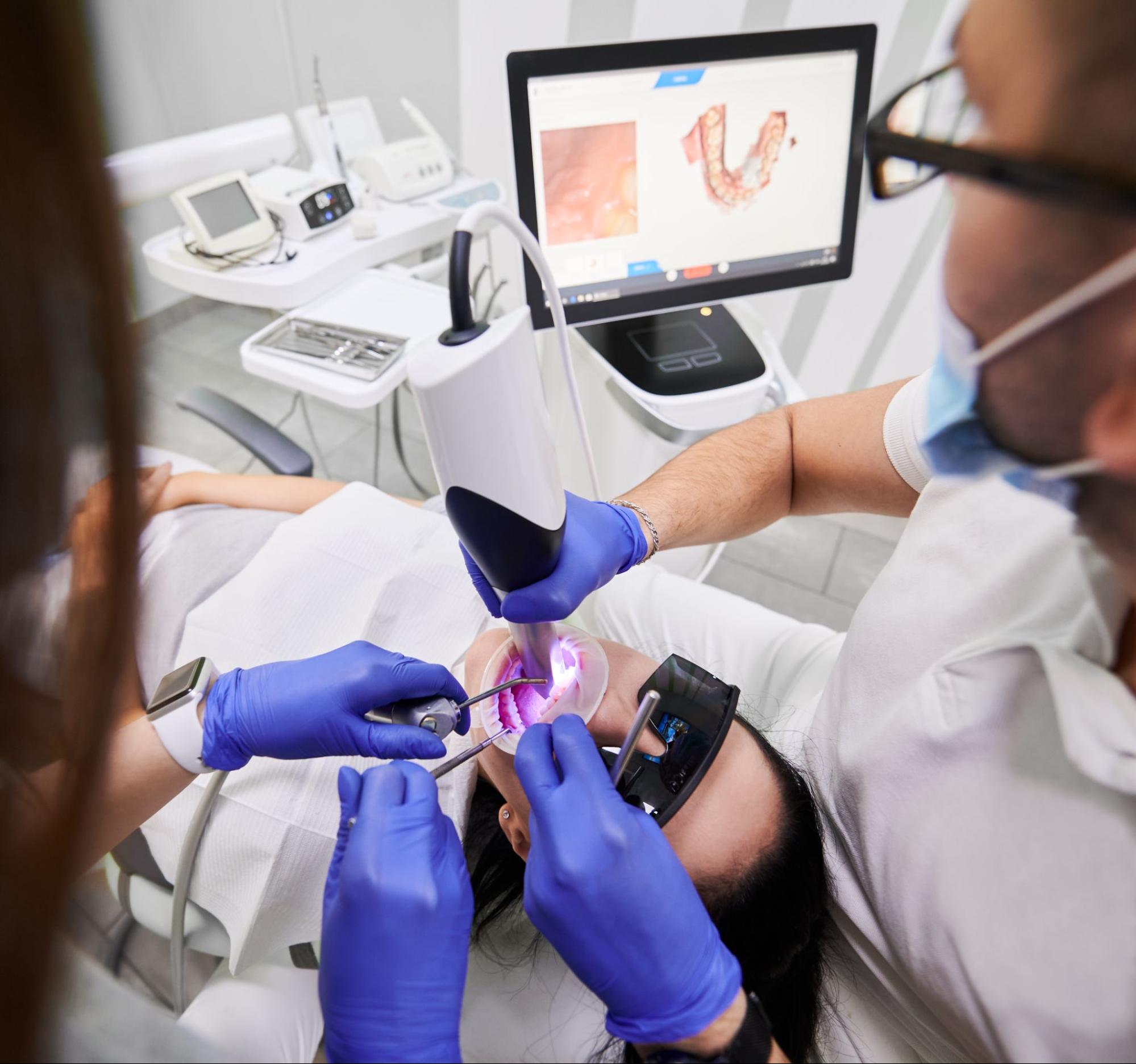 A dentist uses an intraoral scanner to check a patient's mouth before applying dental sealants. 