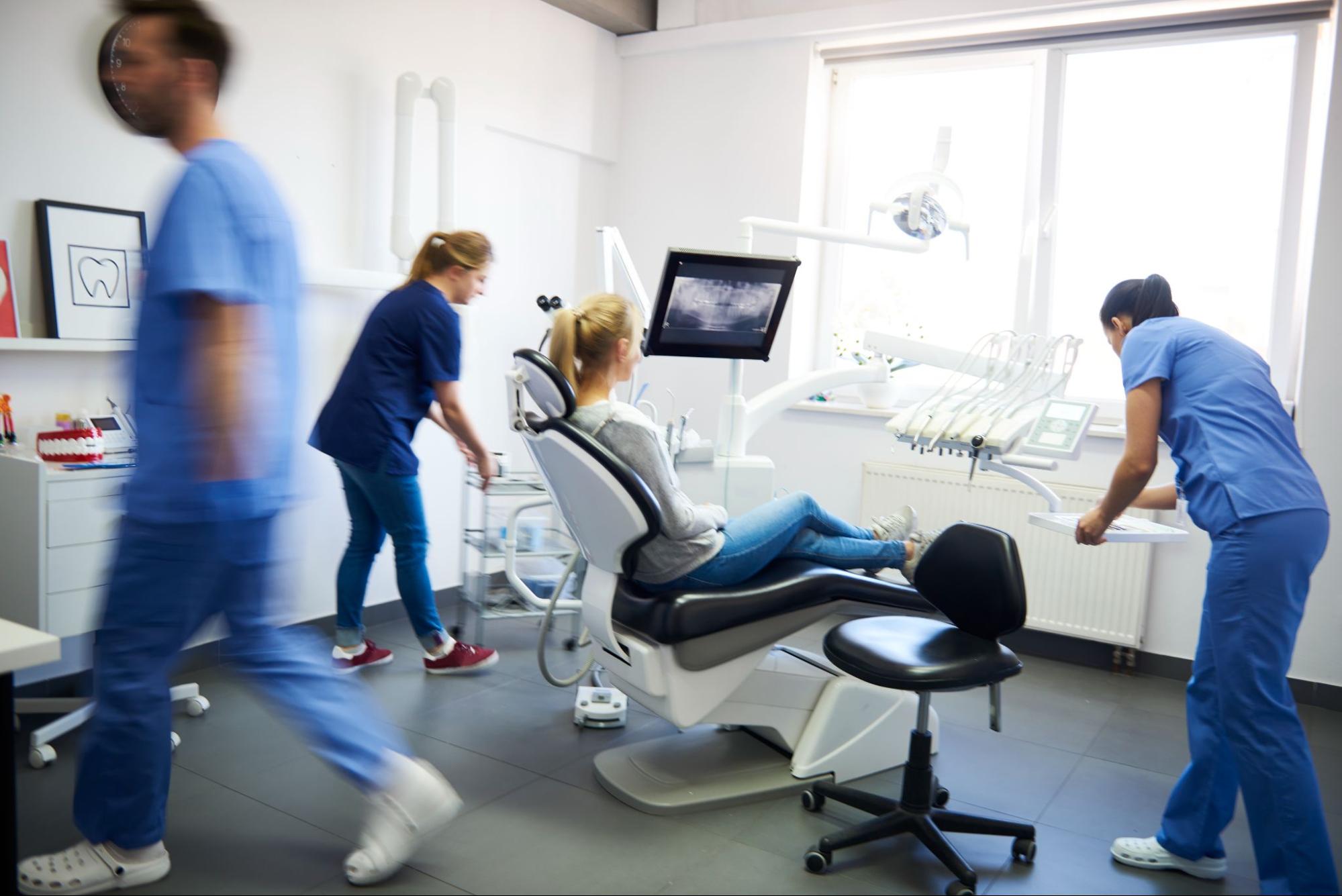 A patient looks at her dental X-ray while the dentist and assistants prepare for the treatment.